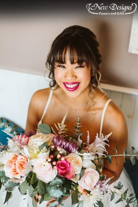 A grinning Bride holds a bouquet of Vibrant hues, White Peonies, Lavender fuji mums, Bright pink miniature roses, peach berries, blush ranunculus, with explosive stems of baby and silver dollar eucalyptus